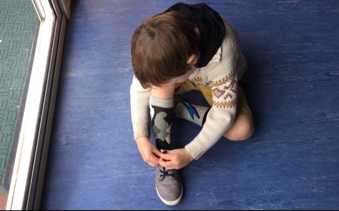 Rockingham Montessori male student seated on the floor tying his shoelace