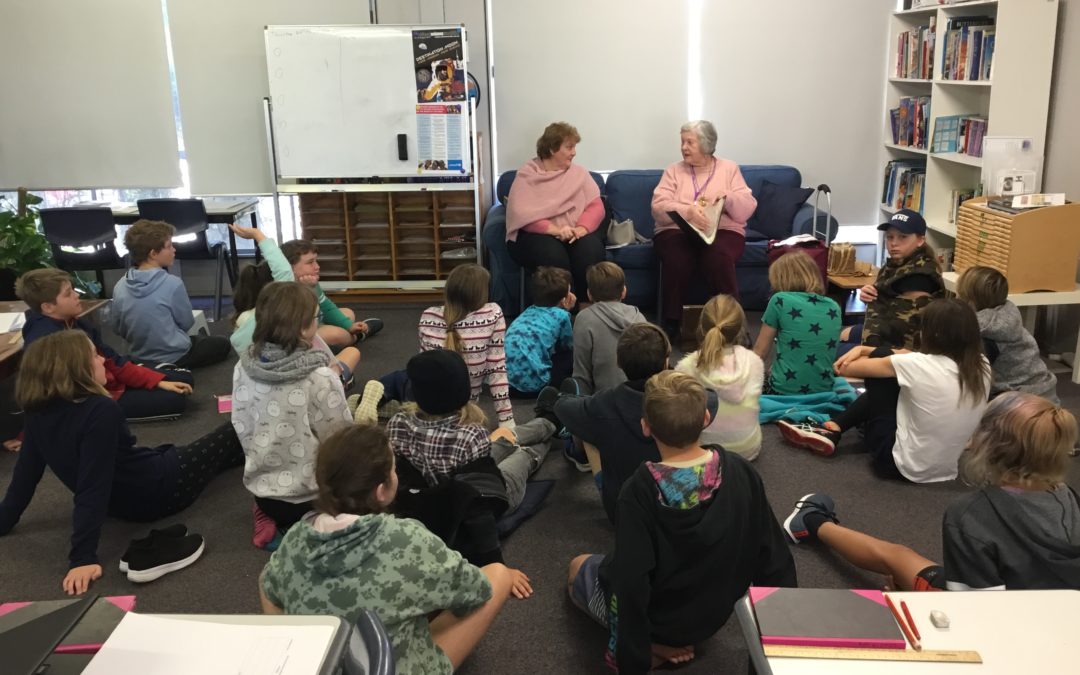 Rockingham Montessori students seated on the ground while listening to two elder women during the RMS Senior Storytellers Visit