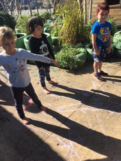 Rockingham Montessori Male and Female students drawing their shadows with chalk in the RMS garden