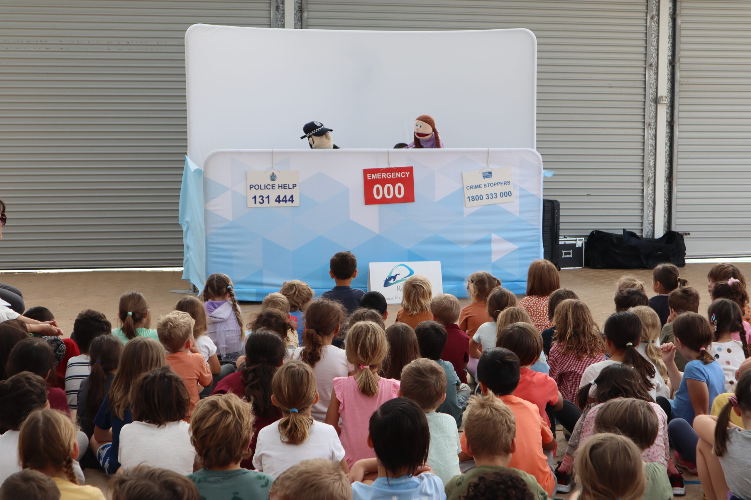 Rockingham Montessori students seated on the ground while watching a puppet show at the Constable Care warehouse